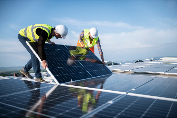 Dva pracovníci s přilbami drží solární panel na střeše Dva pracovníci s přilbami drží solární panel na střeše