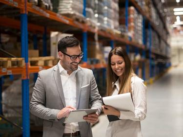 Two people walking through a warehouse looking at papers