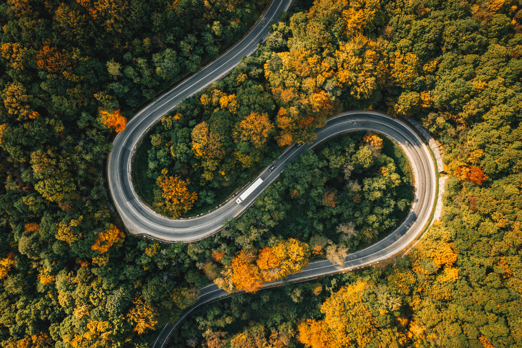 essentials-mobility-left.jpg An electric truck driving on a winding road through fall trees