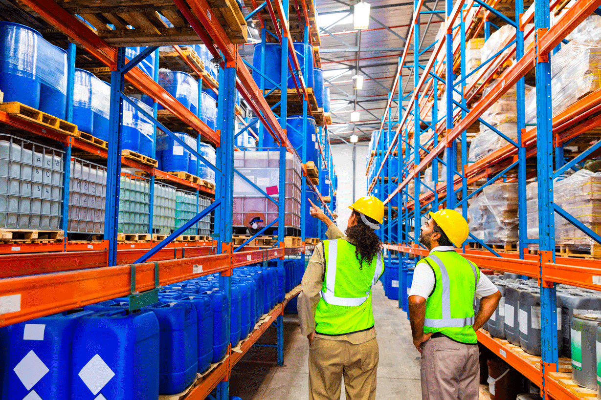 Two people walking in a warehouse in safety vests and hard hats Two people walking in a warehouse in safety vests and hard hats
