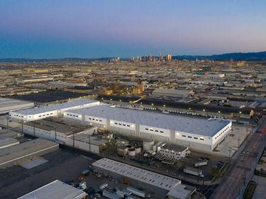 Aerial view of Prologis Vernon Business Center with Prologis globe logo on corner of building, located in Los Angeles, California with LA in city skyline in the distance.